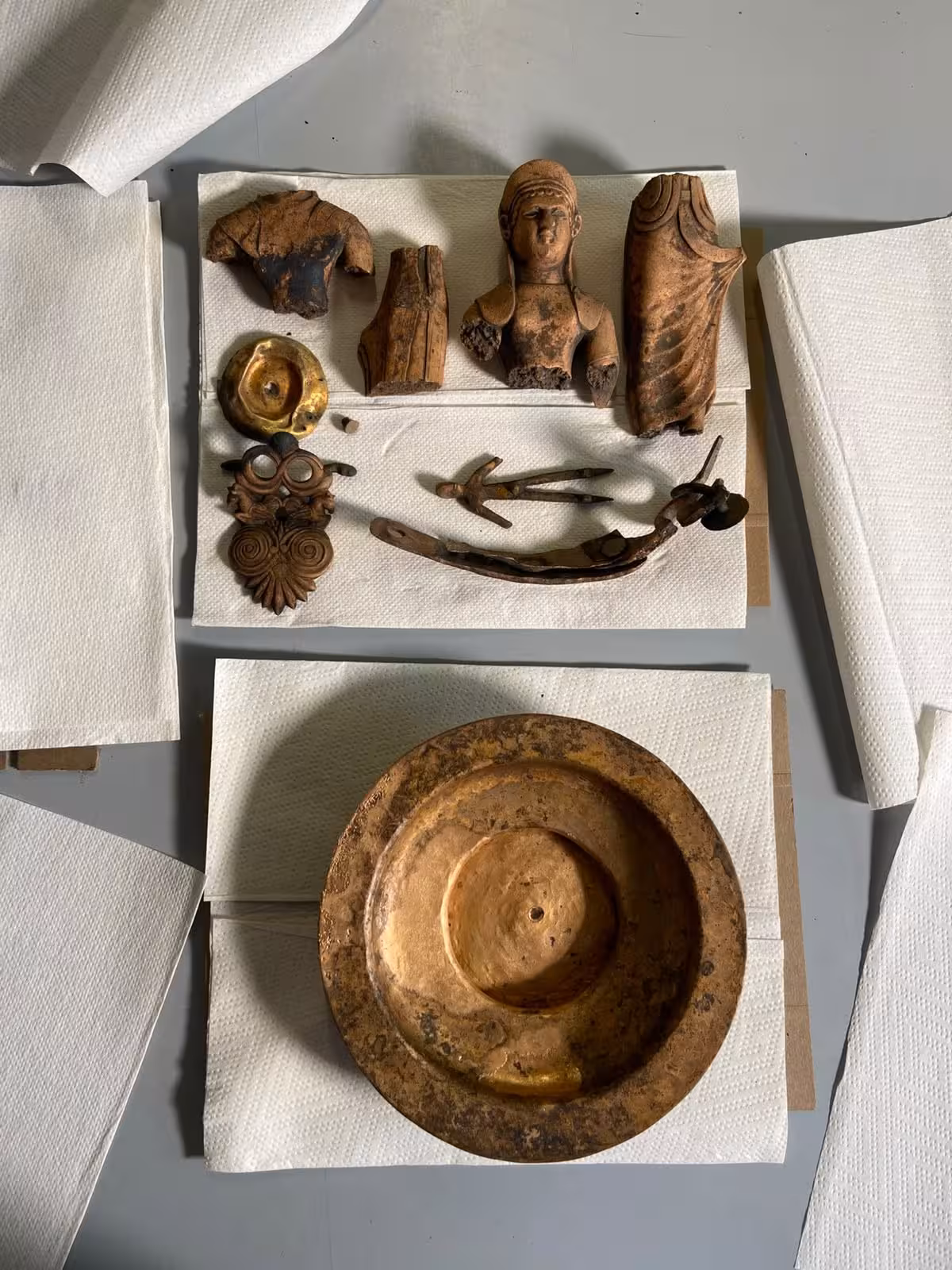 Images from an archaeological excavation showing bronze relics on paper towels.