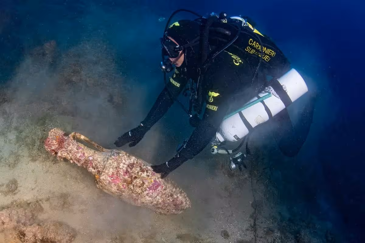Carabinieri Diver Reaching Toward A Roman Amphora Covered In Pink Coralline Algae And Marine Concretions On The Seabed Off Camogli