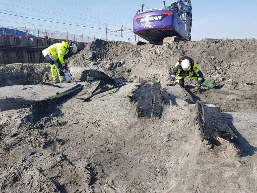 Two people dressed in yellow are digging out remains that appear as small hills or similar underground.