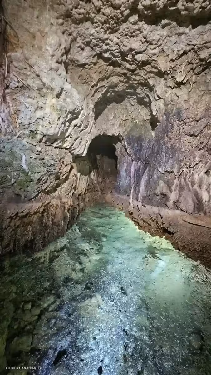 A Narrow Underground Passage Carved Into Natural Rock, With Ancient Stone Walls Surrounding A Shallow Pool Of Clear Turquoise Water.