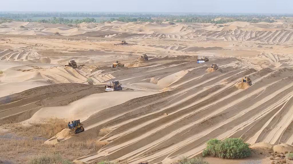 Aerial view of tractors flattening sand dunes in China's Taklamakan Desert.