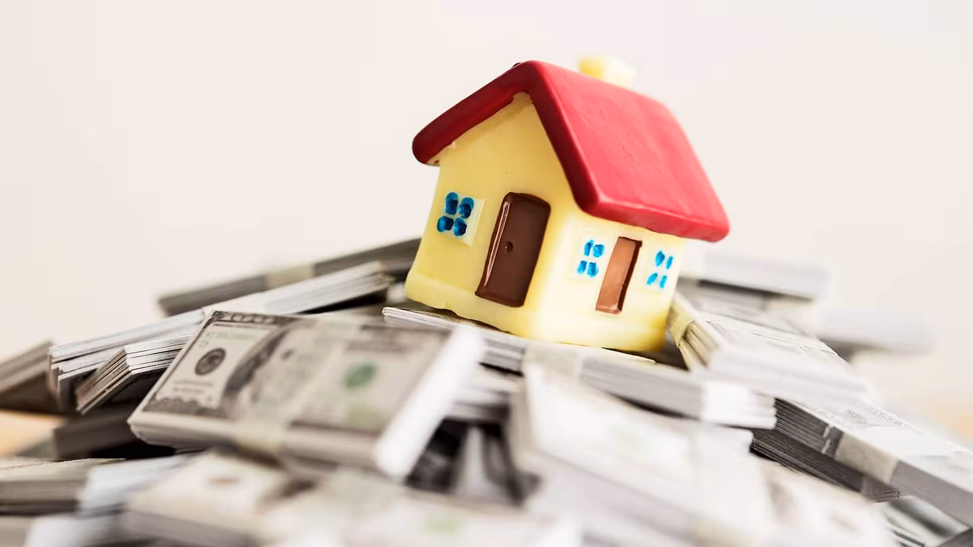 A small model of a house sits on stacks of cash.