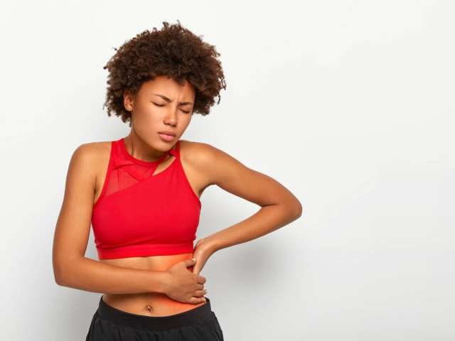Free photo dissatisfied woman holds aching hip, has kidney inflammation, touches location of pain near ribs marked with red dot, wears sport bra.