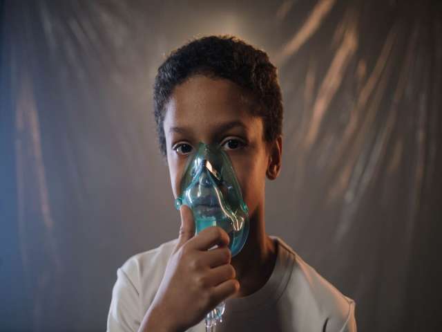 A Boy in White Shirt Holding Green Oxygen Mask.
