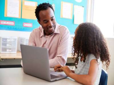 Teacher working with elementary school girl at laptop