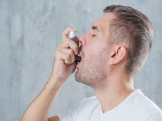 Free photo portrait of a young man using asthma inhaler against grey background.