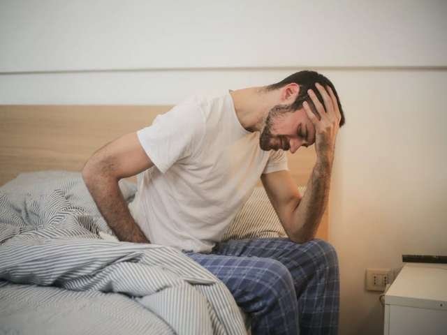 Young man in sleepwear suffering from headache in morning.