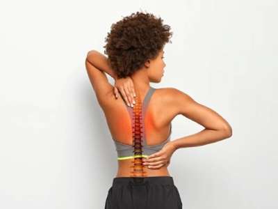 Faceless curly woman suffers from spine pain, wears sport bra, shows location of inflammation, isolated on white background