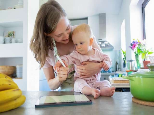 Mom and baby daughter cooking together at home, watching recipes on tablet. Child care or cooking at home concept.