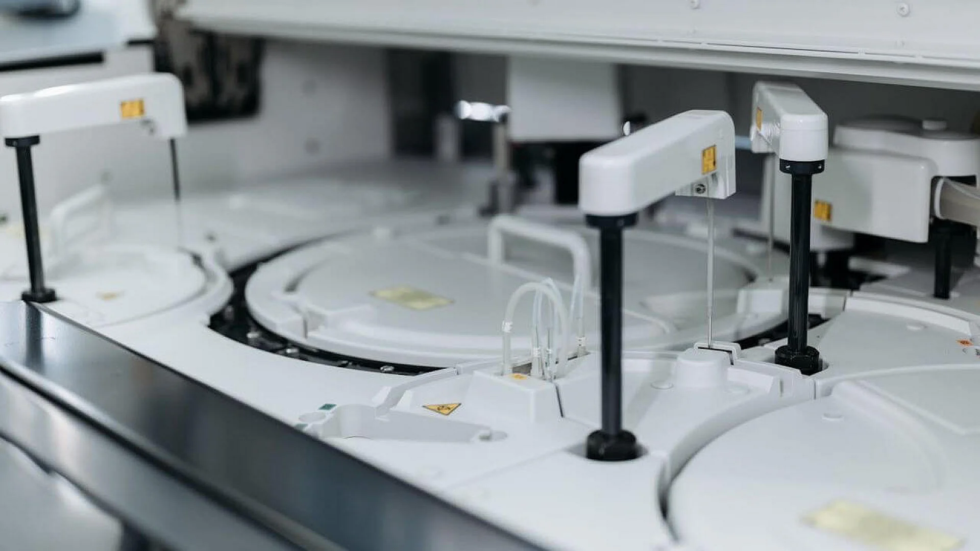 A close-up of a clinical laboratory analyzer showing white robotic probe arms and a circular reagent carousel.
