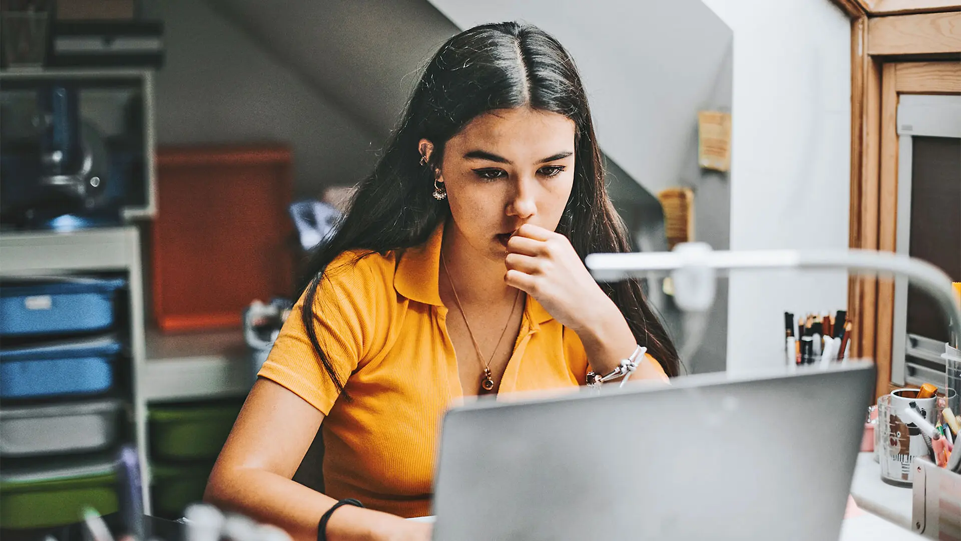 A college student thinks while looking at her laptop in a dorm room.