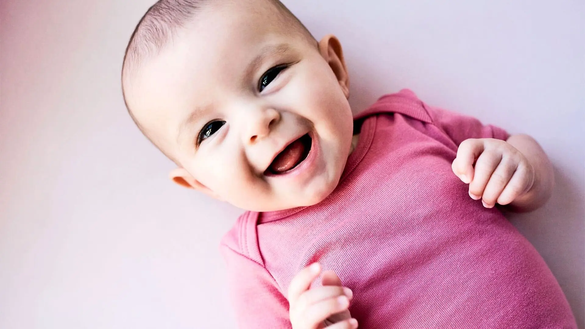 A baby in a pink onesie smiles at the camera.