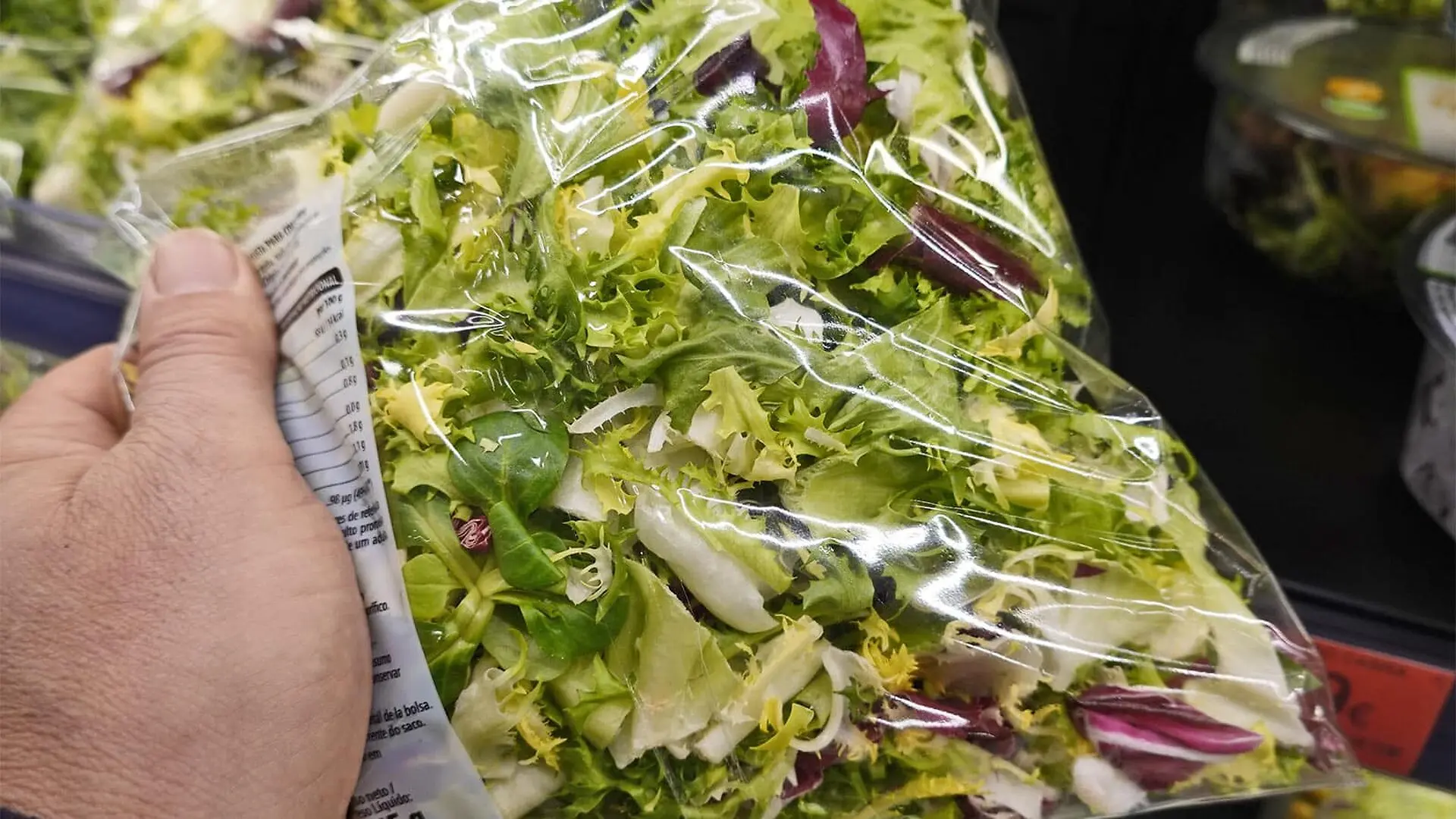 A person holds a bag of lettuce at the grocery store.