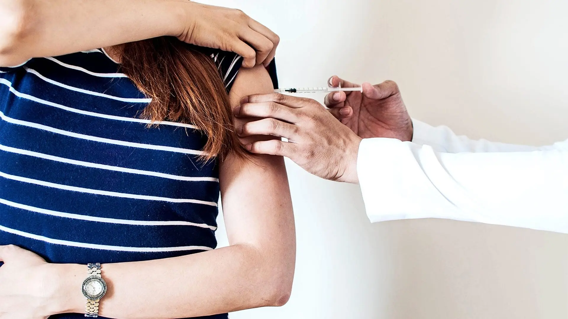 A doctor in a white coat gives a patient a flu shot in her arm.