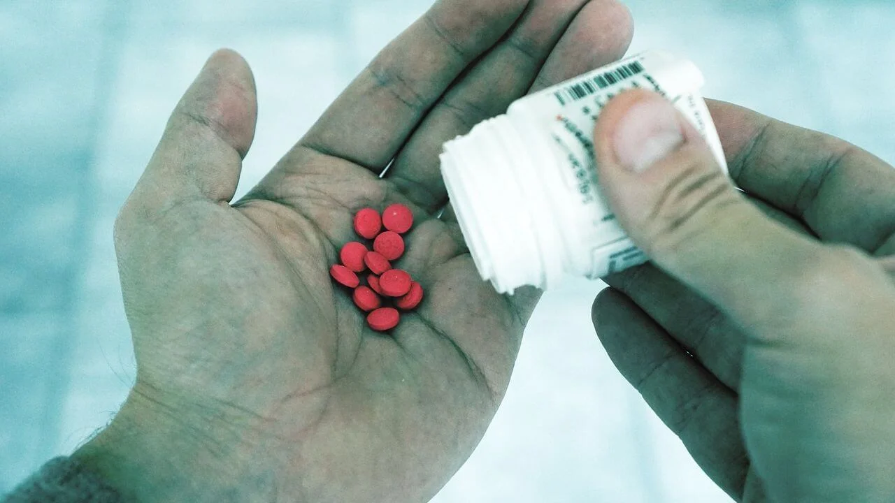 Person pouring red pills from a white prescription bottle into the palm of their hand.