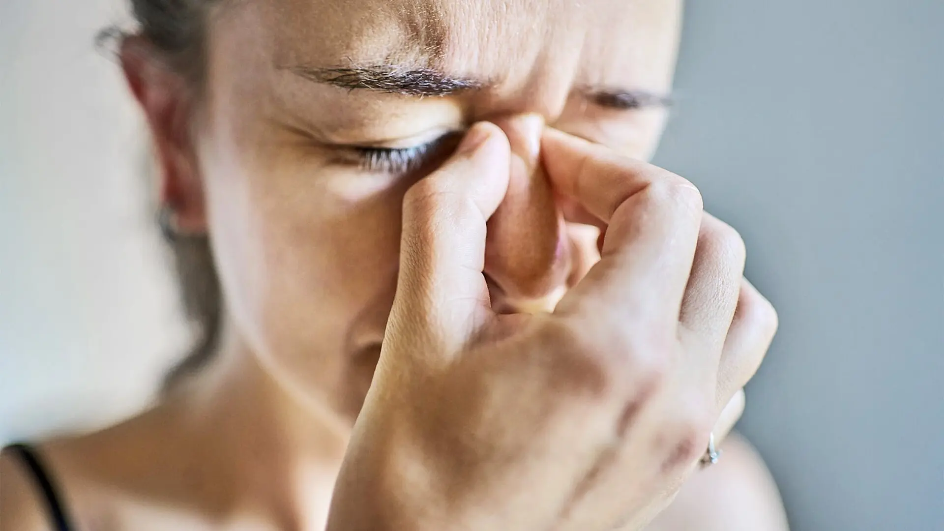 A woman holds the bridge of her nose and looks stressed.