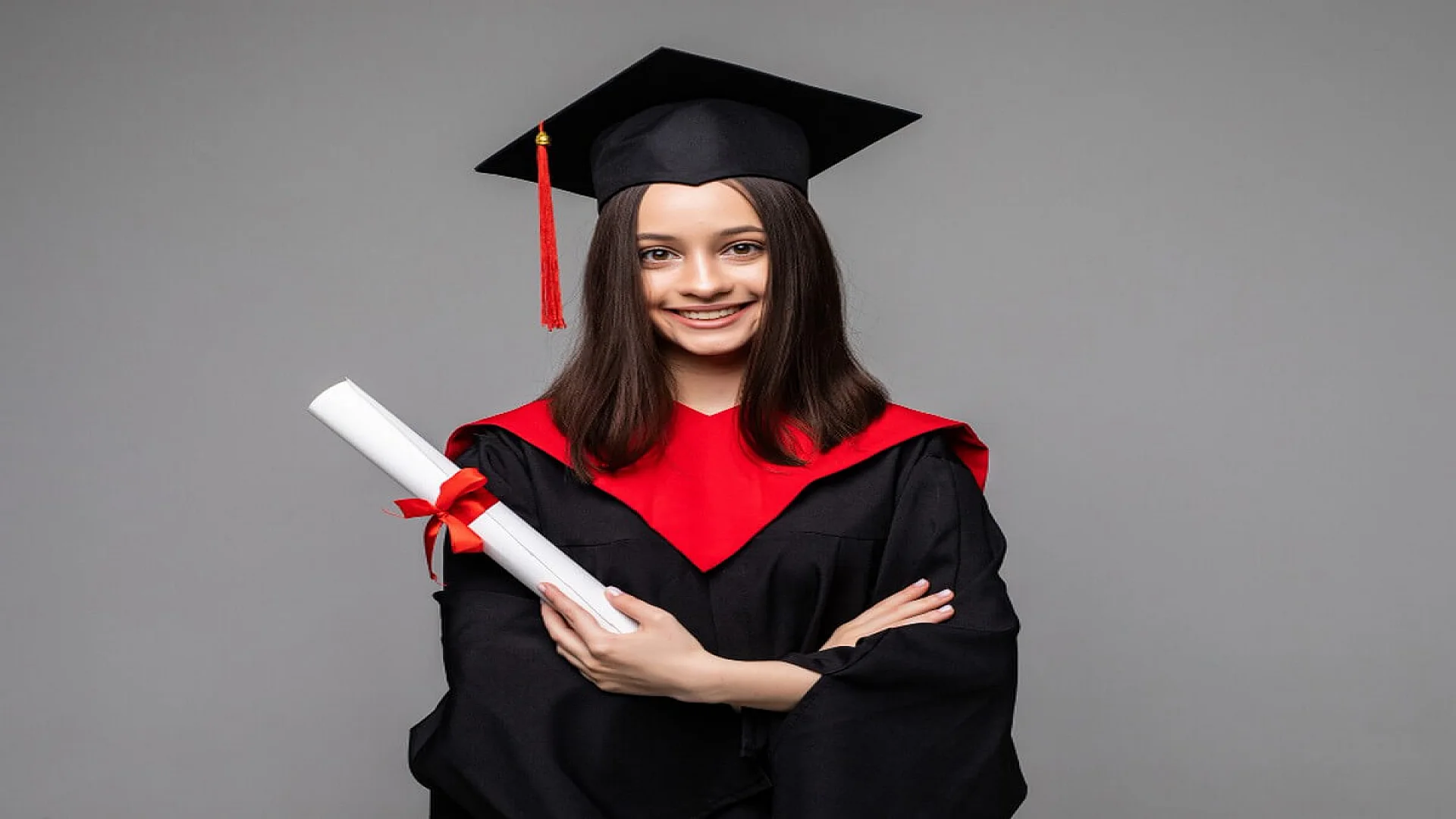 Happy student with graduation hat and diploma on grey background.