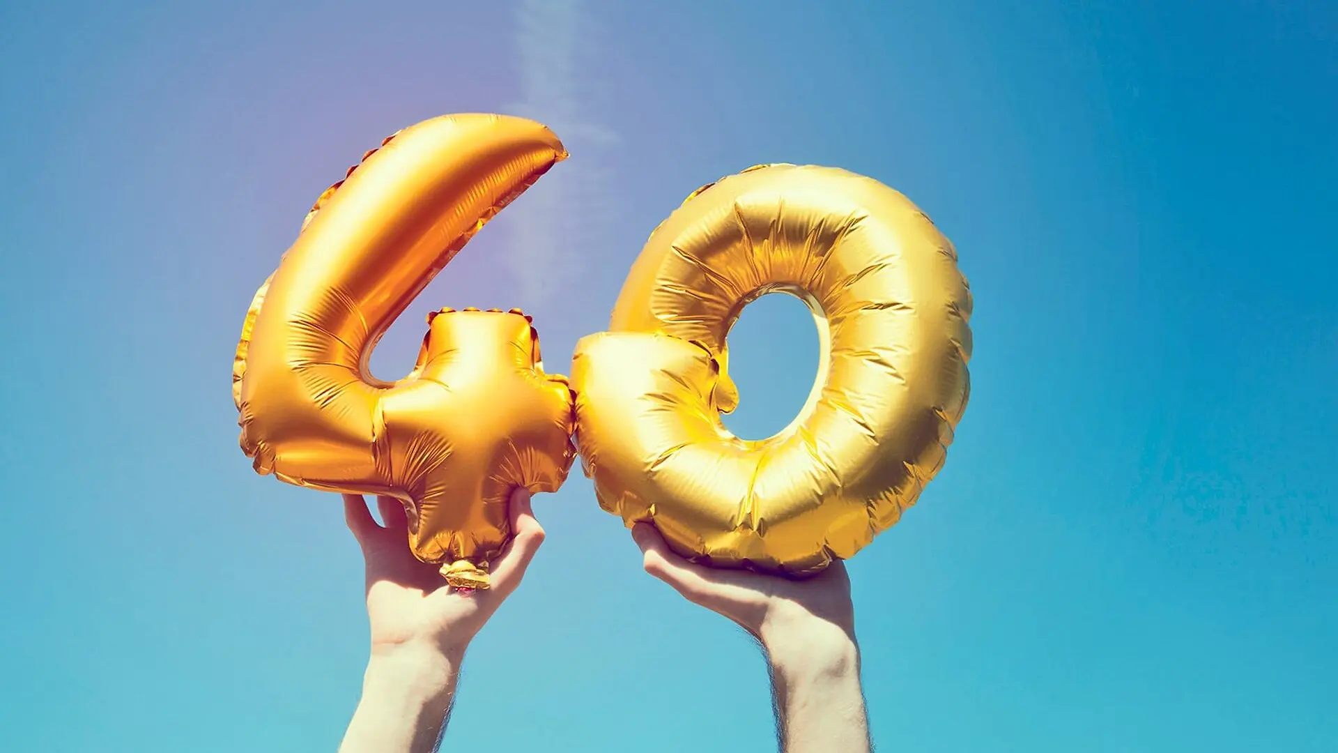 A person holds up balloons of a 4 and a 0.