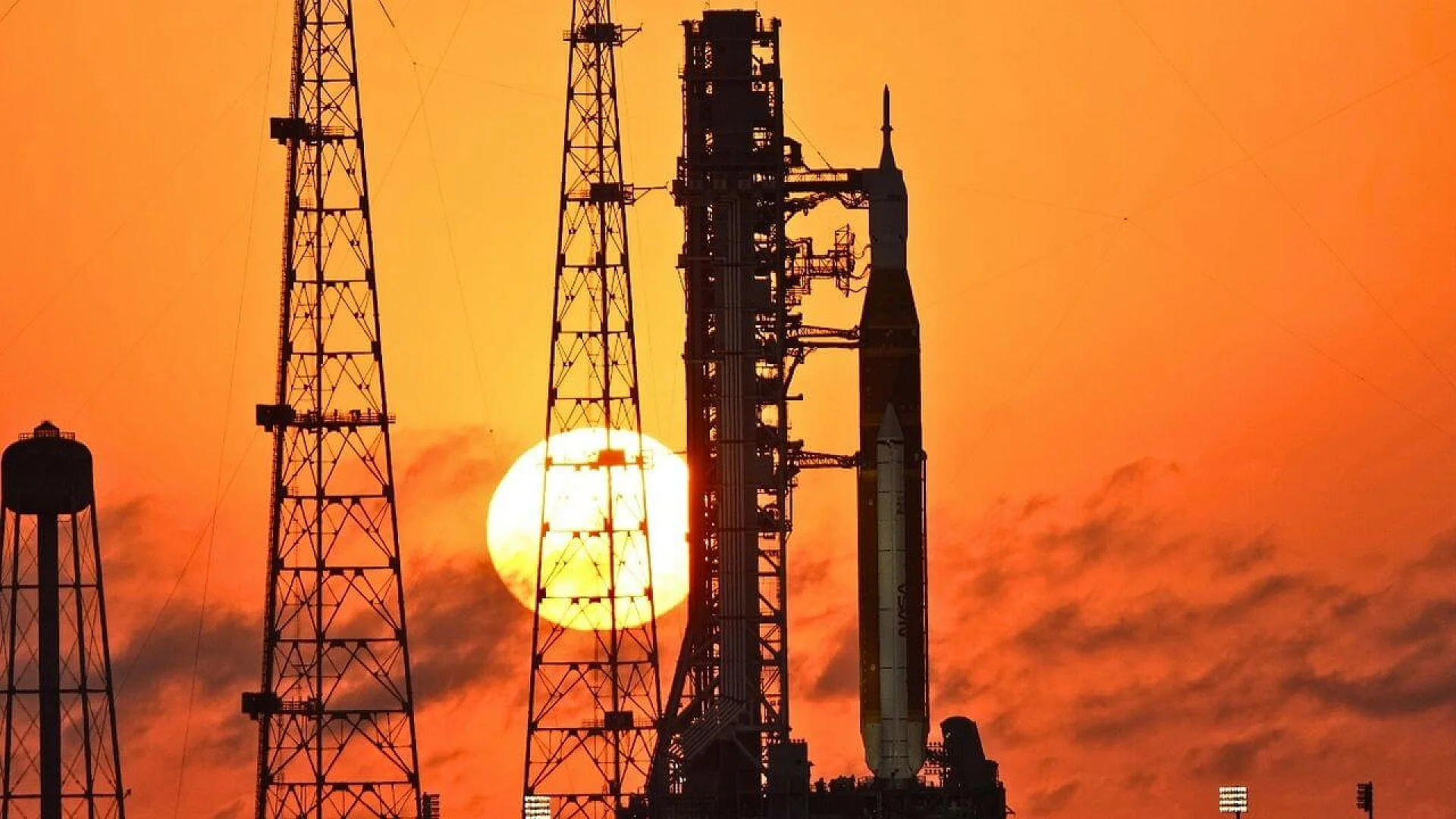 NASA’s Space Launch System rocket and Orion spacecraft stand on Launch Complex 39B at Kennedy Space Center, silhouetted against a vibrant orange sunrise with the sun positioned behind the launch structures.