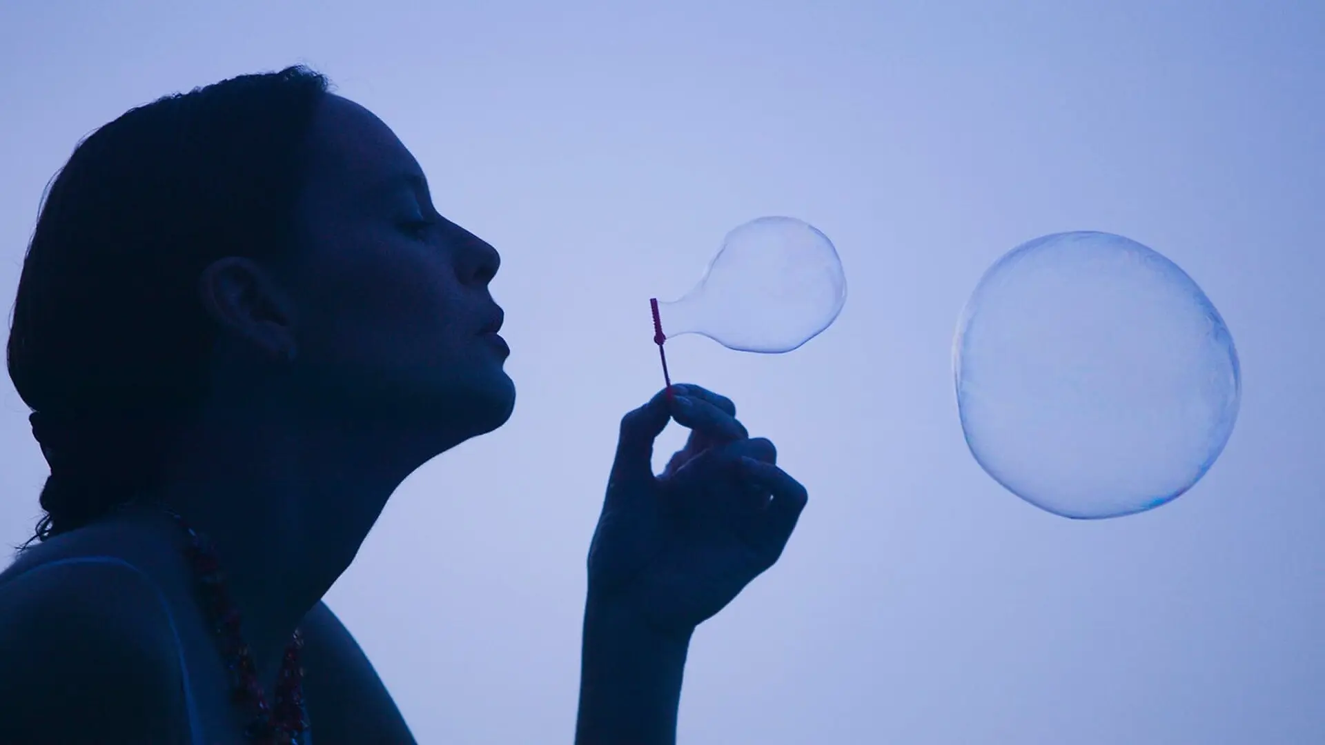 A woman blows bubbles using a small bubble wand.