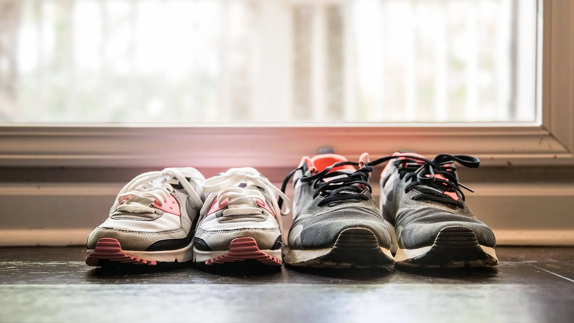 Two sets of running shoes sit unused by a door.