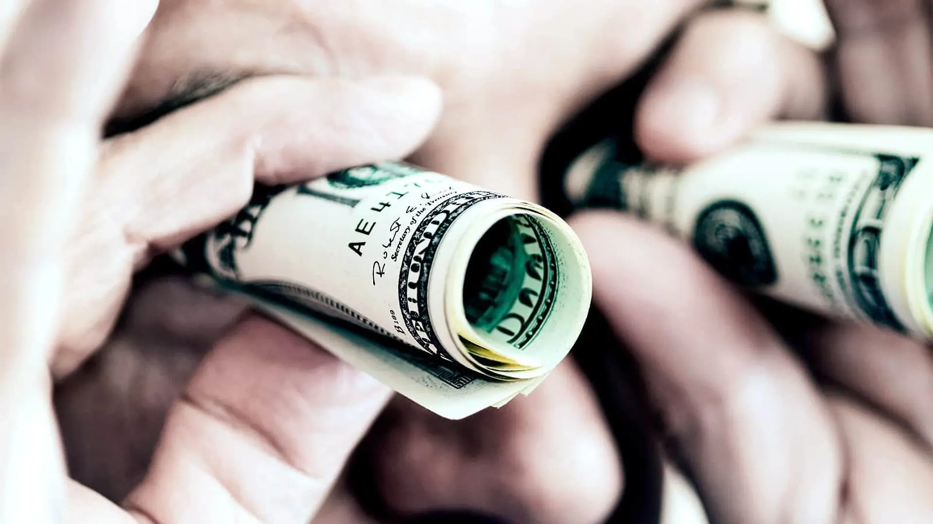 A person holds rolled up dollar bills up to their eyes as if they