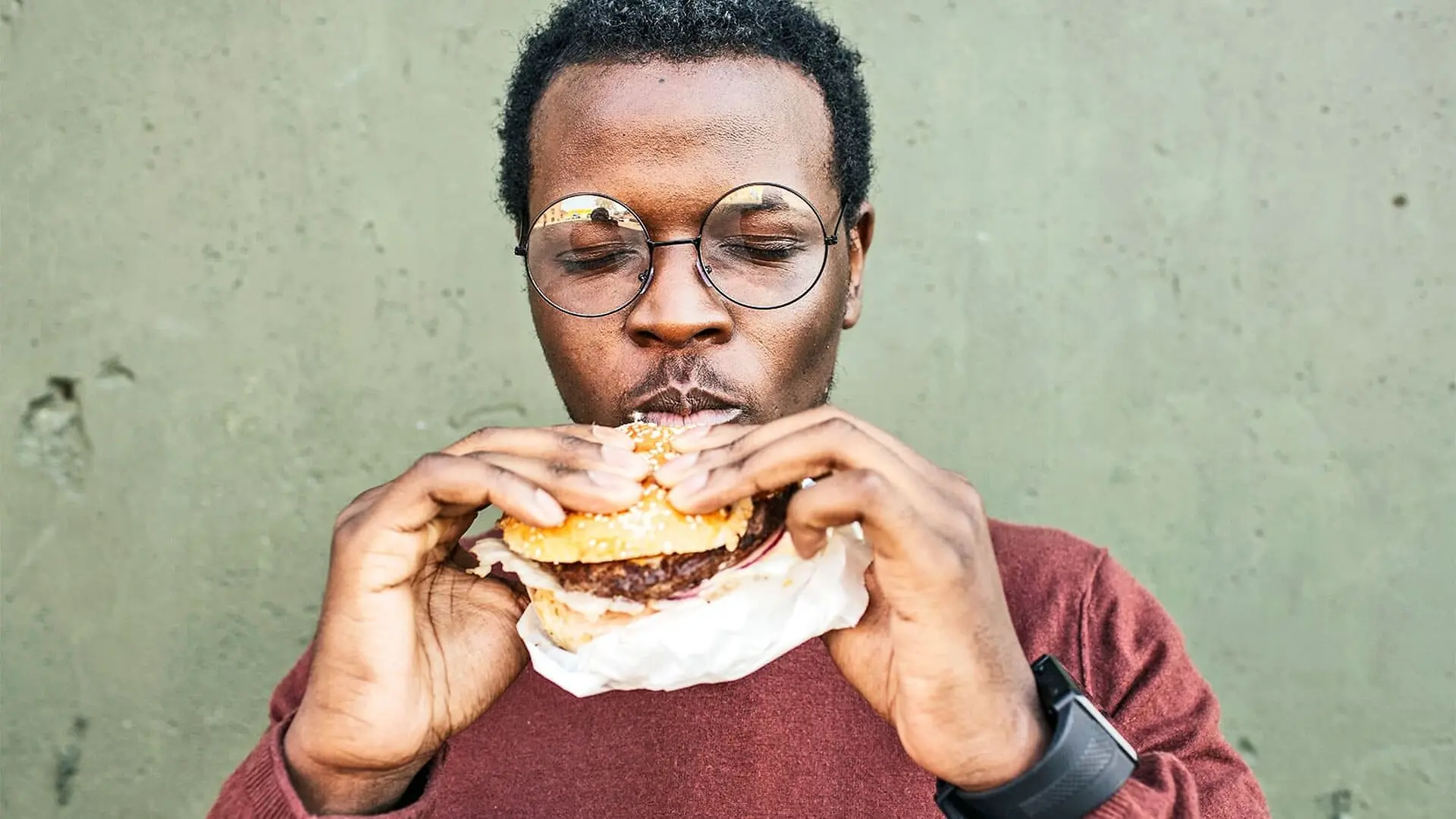 A man closes his eyes while enjoying a bite of a cheeseburger.