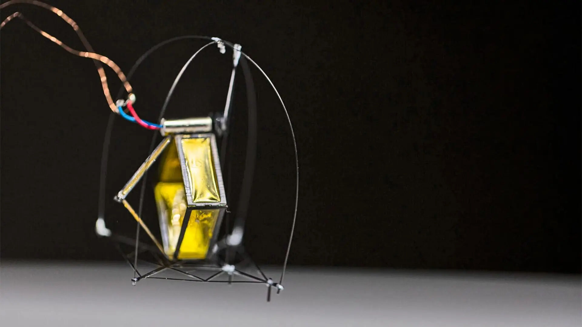 The small robot with a wiry frame hops above a white surface.