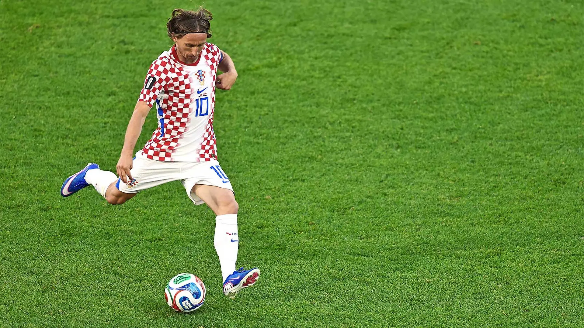Modric lifts his right leg to kick the soccer ball on a deep green field.