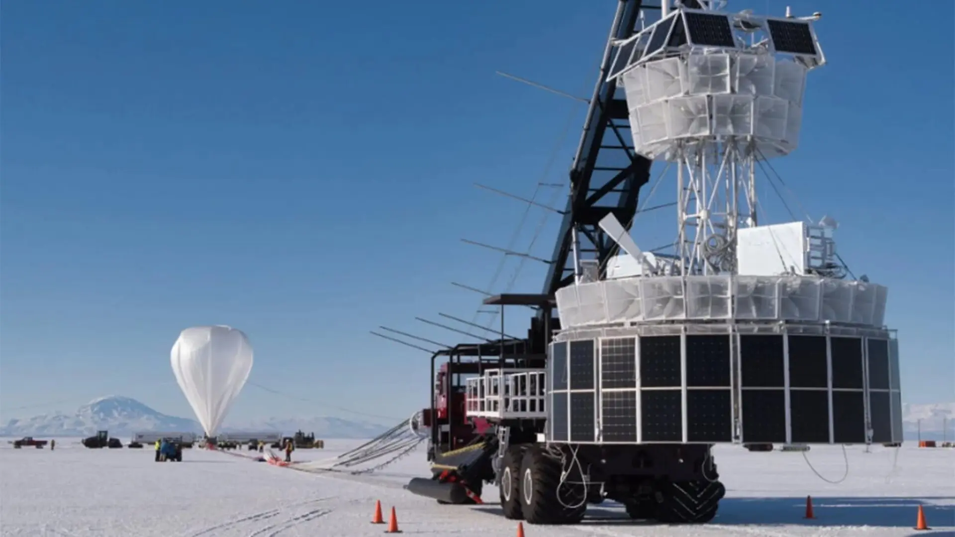 A truck carries large equipment near a balloon ready to take off.