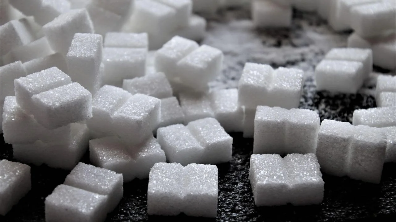 A close-up photograph of several white sugar cubes scattered on a dark, textured surface, representing glucose.
