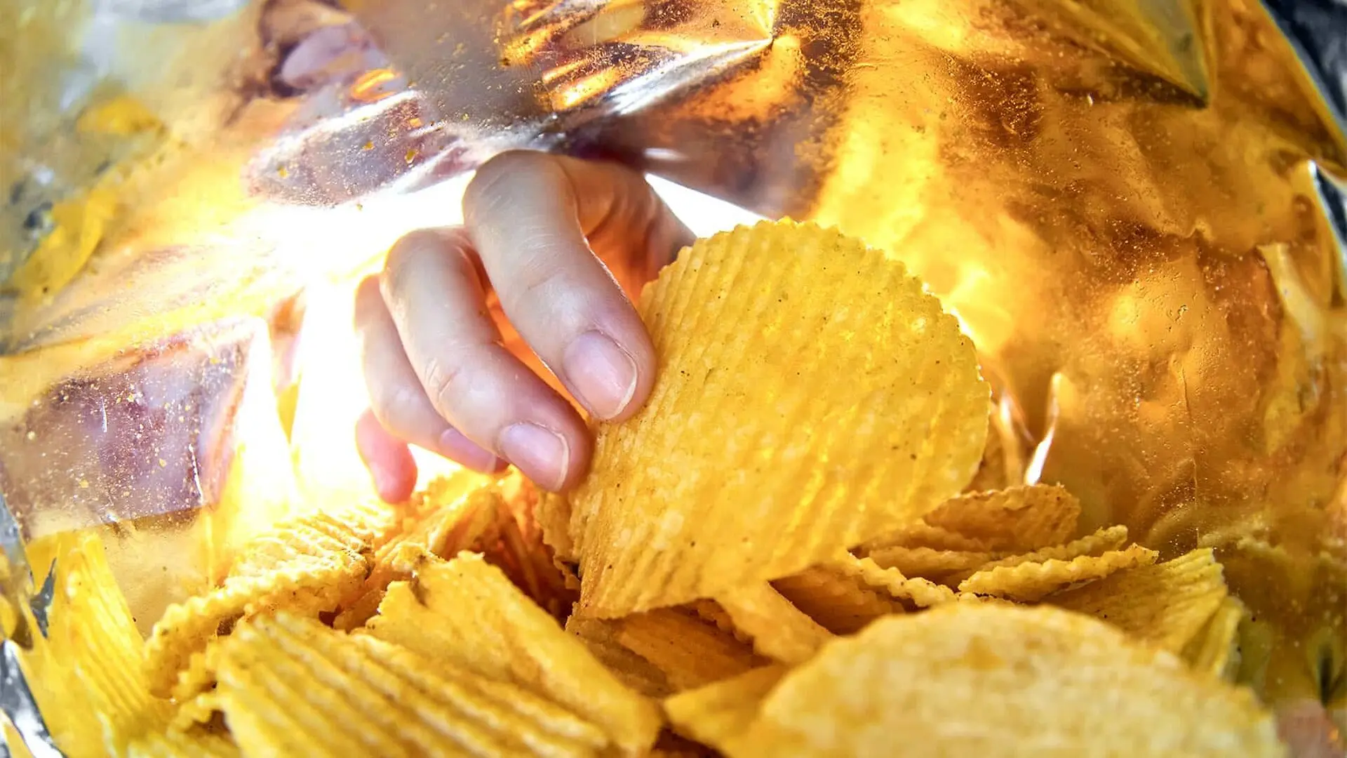 A hand reaches into a potato chip bag.