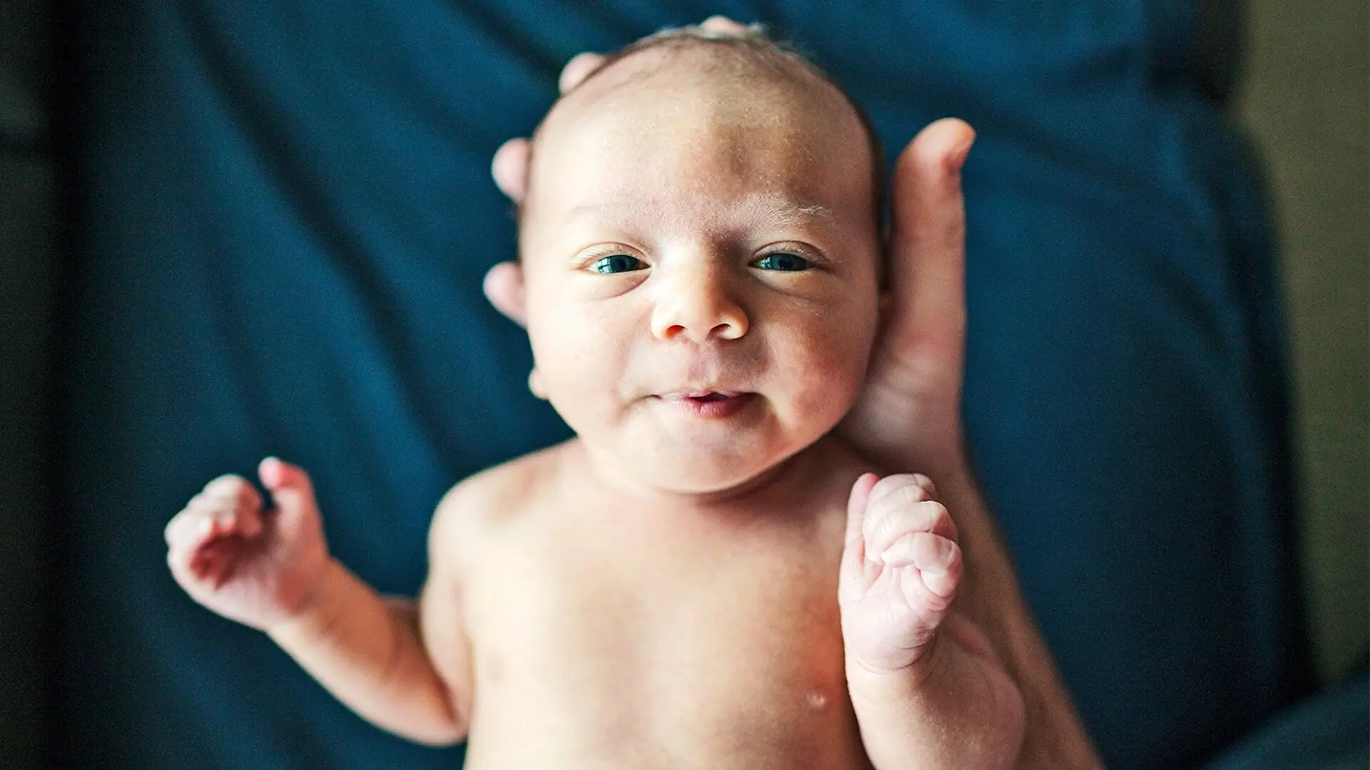 A person holds a newborn baby who is looking up at the camera.