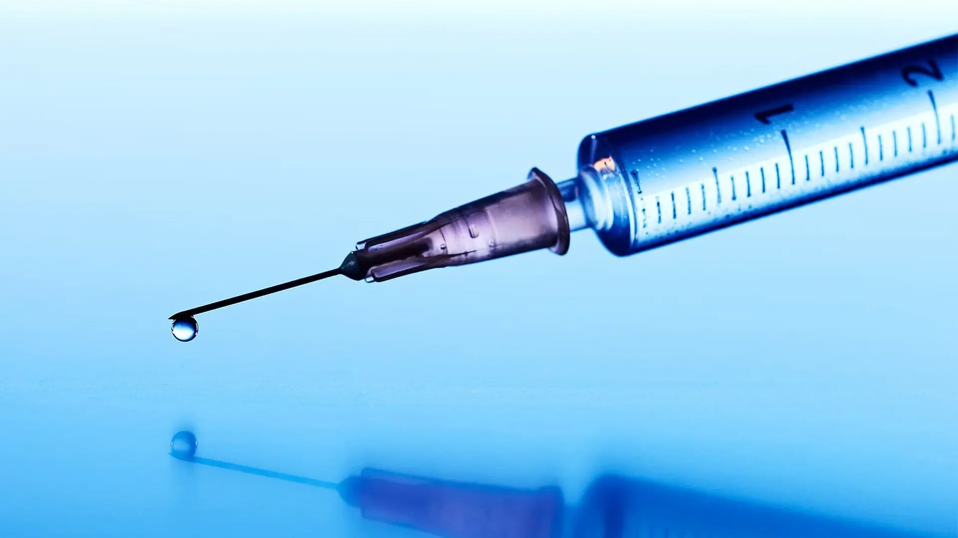 A syringe with a drop of vaccine coming out of the needle.