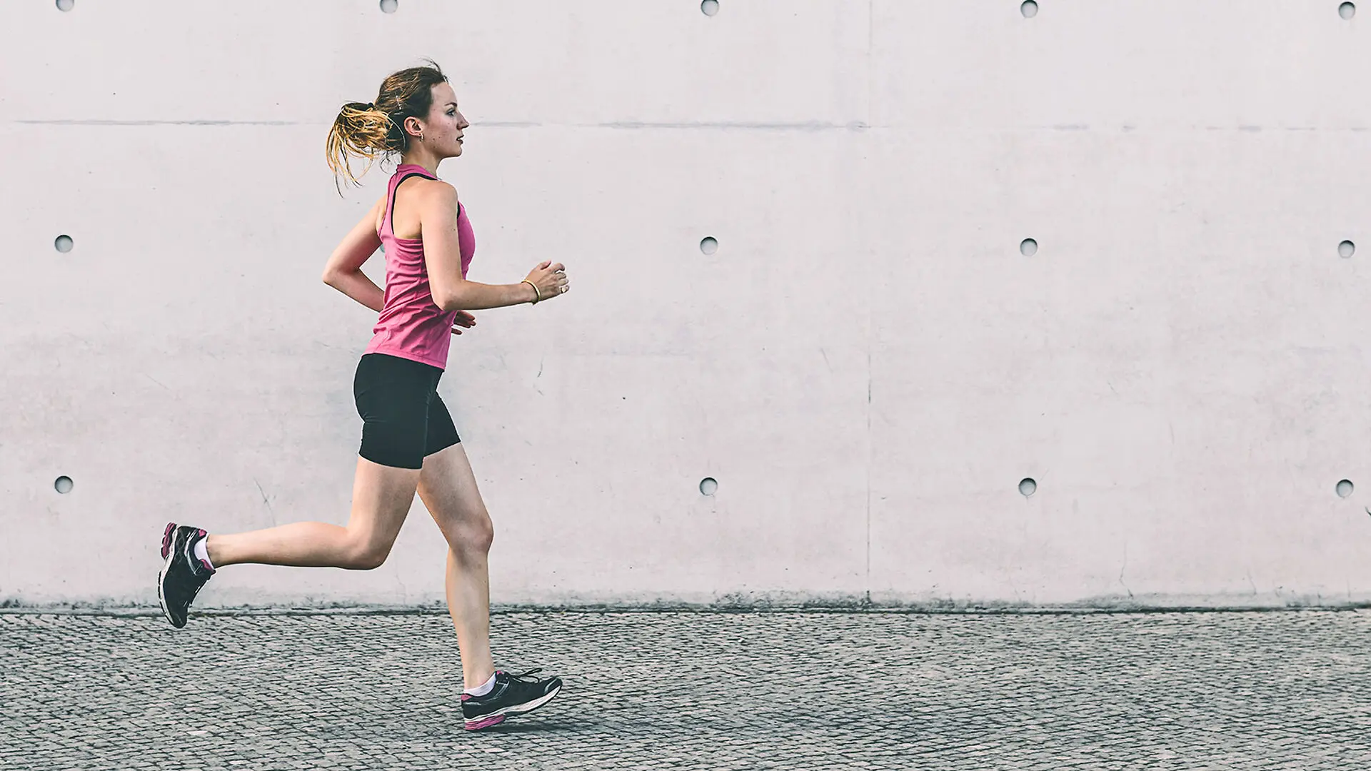 A woman runs next to a concrete wall.