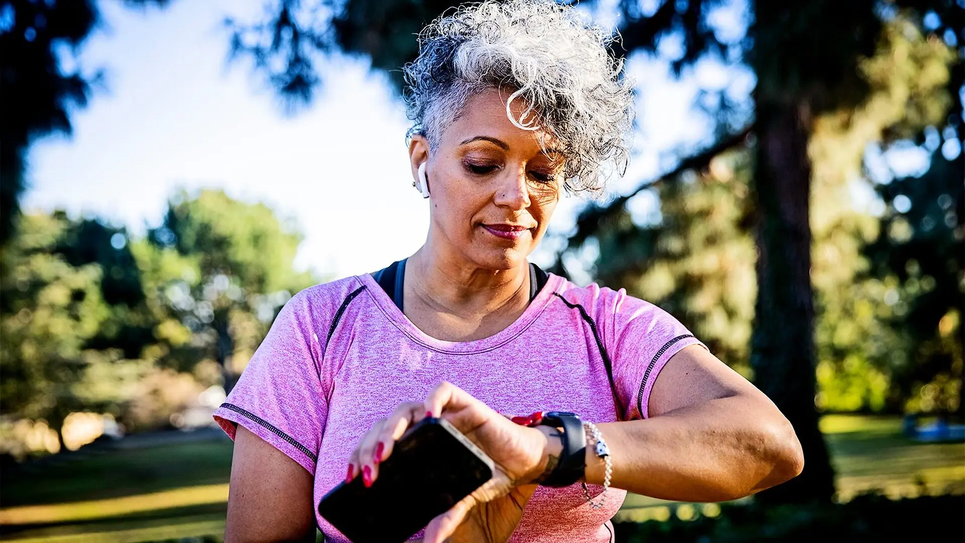 A woman checks her smartwatch while walking in the park.