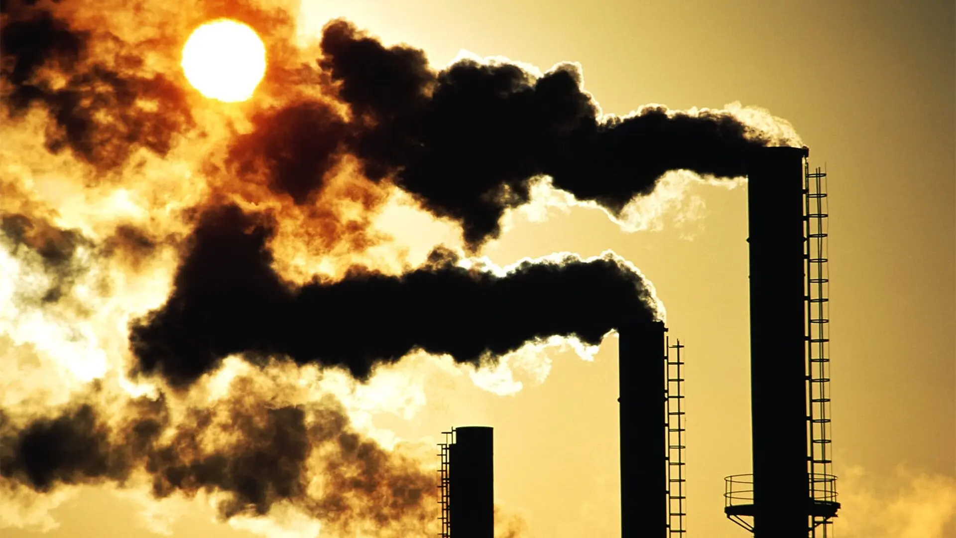 Black smoke pours out of three smokestacks at sunset.