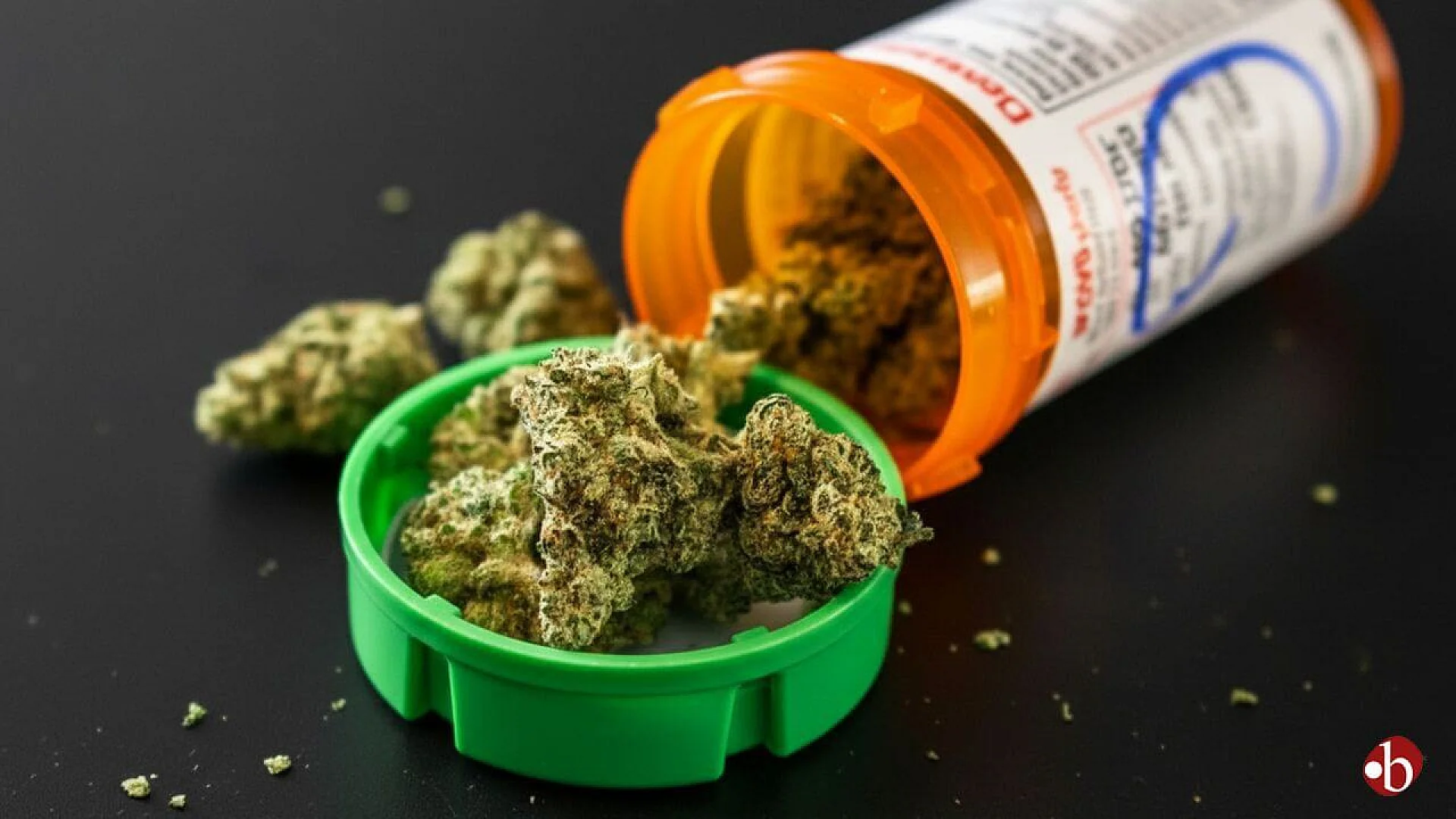 Dried cannabis flowers spilling out of a prescription pill bottle onto a dark background.