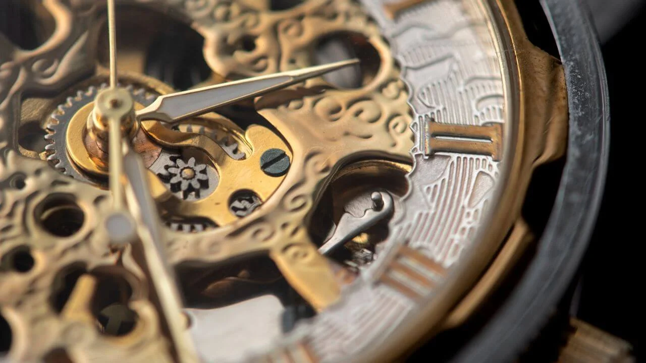 Extreme close-up of a golden skeletonized watch movement with visible gears and hands, contrasting traditional mechanical timekeeping with the new quantum watch concept