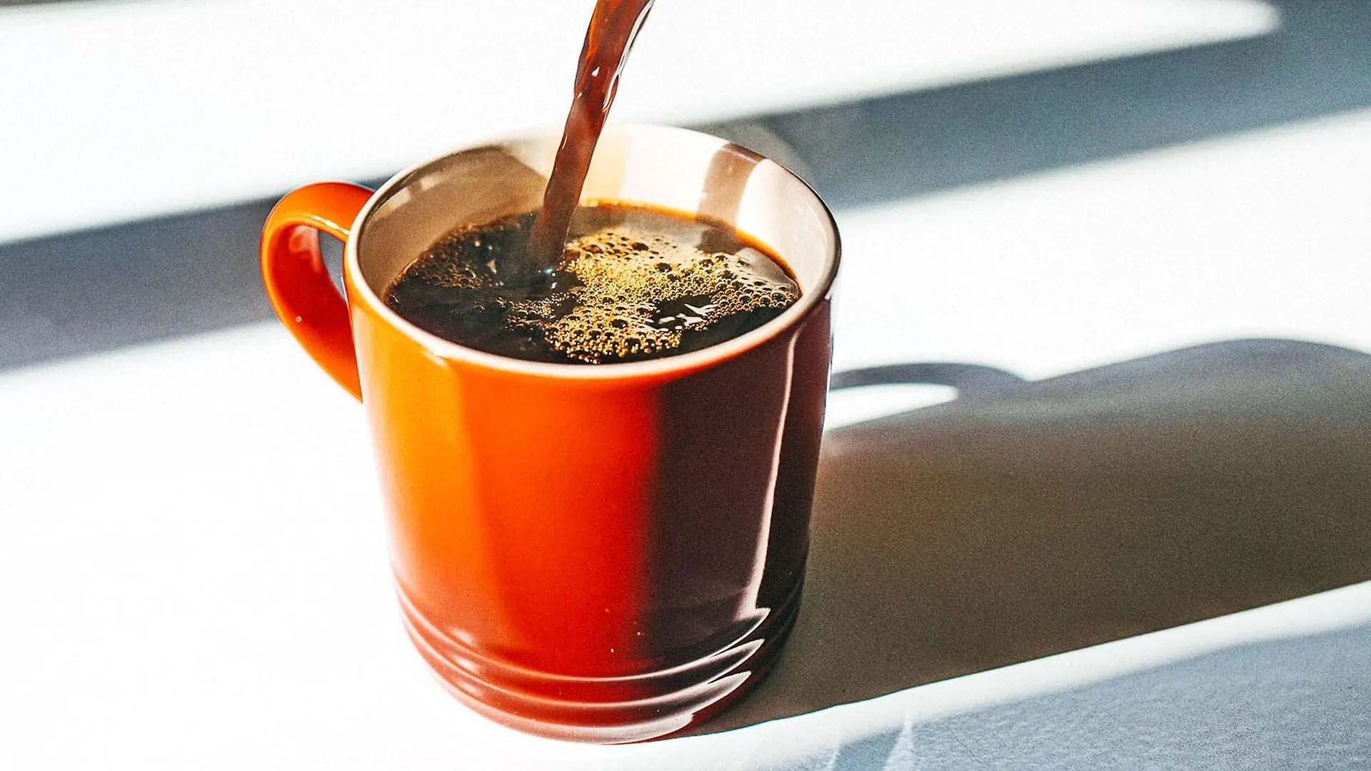 An orange cup of coffee sits on a white surface.