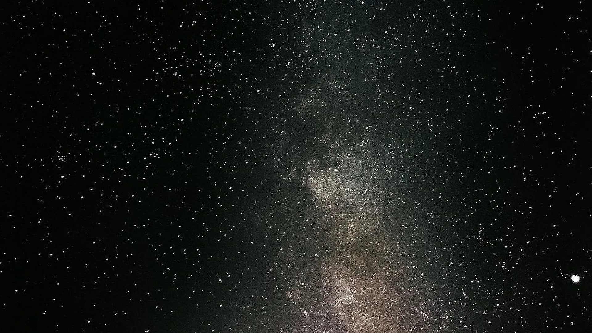 A wide-angle, high-contrast photograph of a starry night sky featuring a dense band of the Milky Way galaxy with thousands of twinkling white stars against a deep black cosmic background.