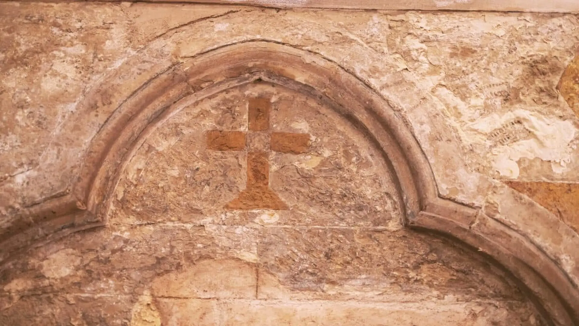 Close Up Of An Old Stone Relief Depicting A Cross Within An Arch Set Into A Damaged Wall Scaled