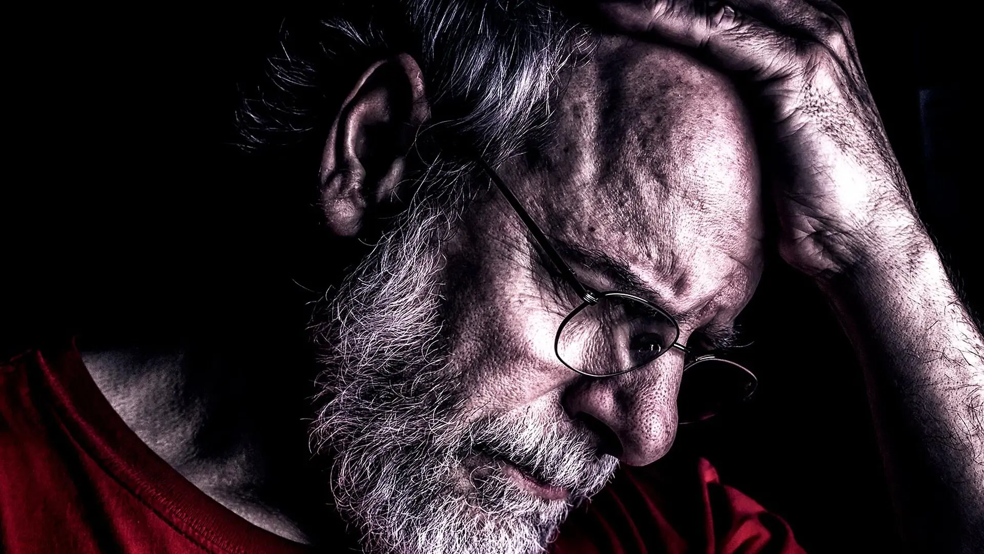 An older man touches his forehead while looking downward.