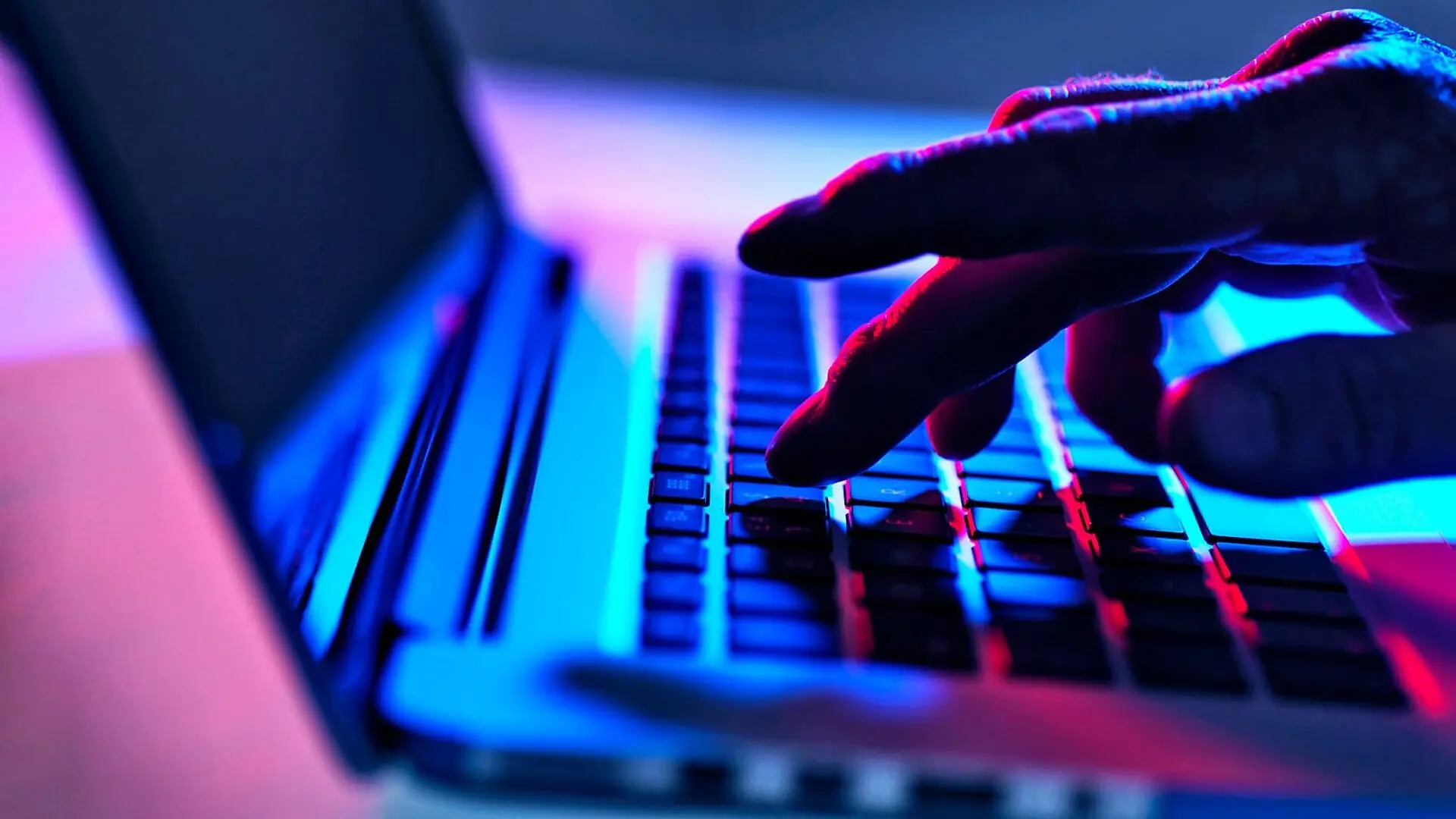 A person types on a keyboard while illuminated in blue and pink light.