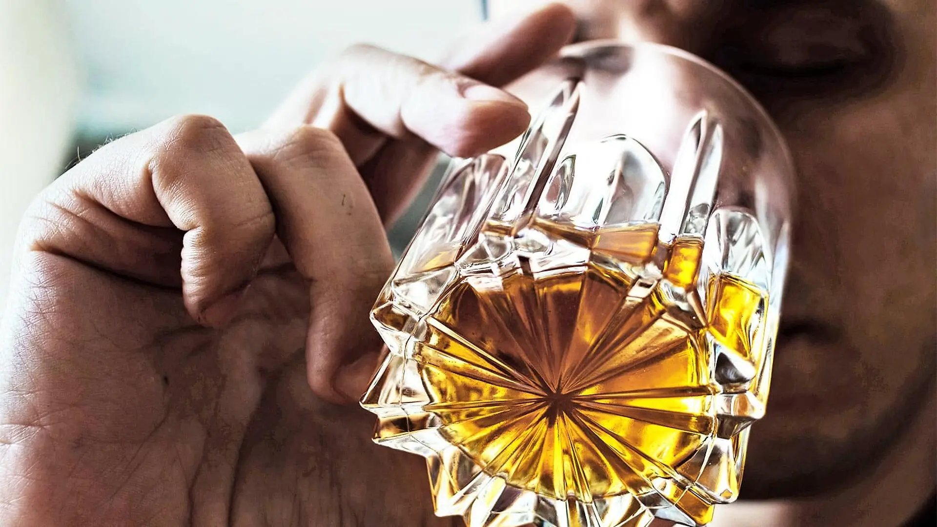 A man sips brown liquor from a glass.