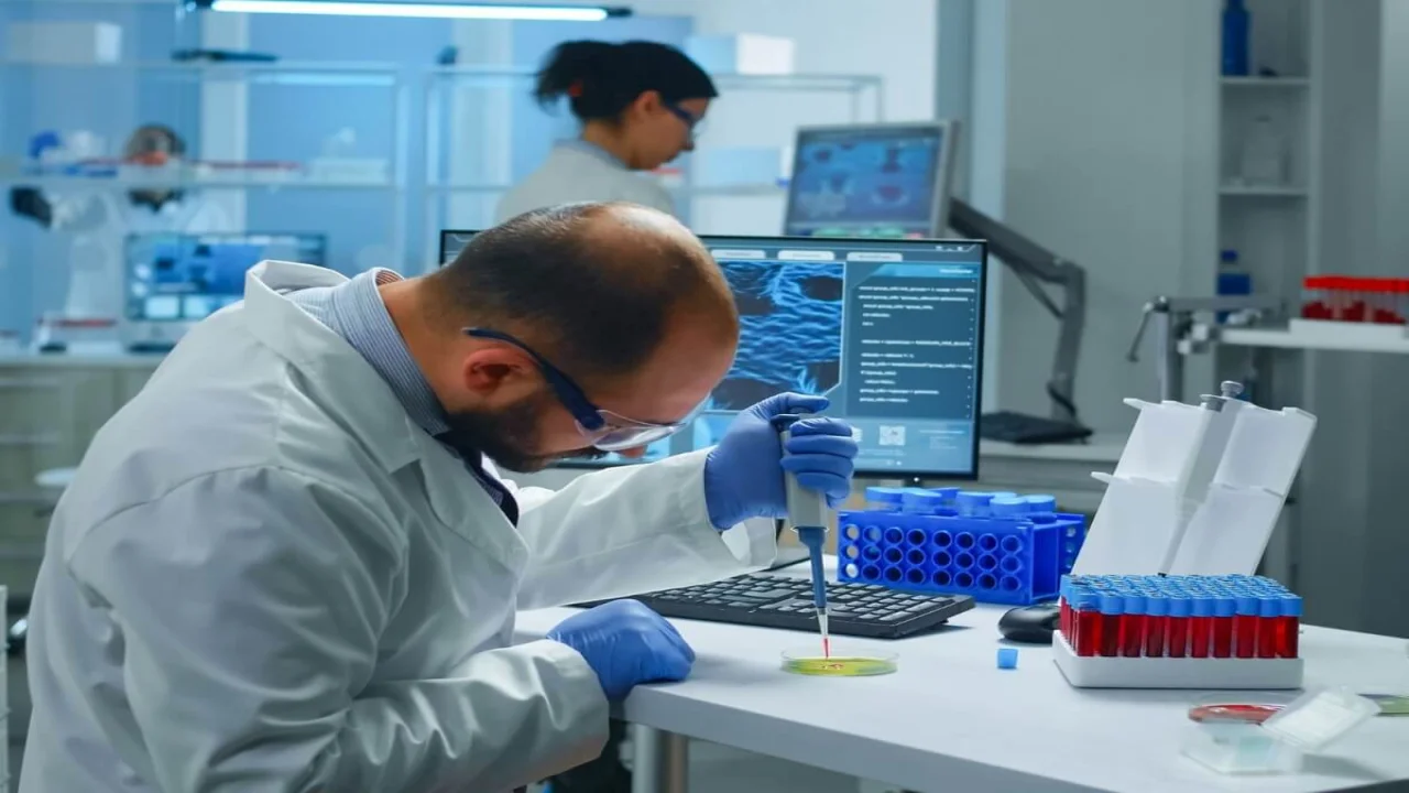 Scientist putting blood sample from test tube with micropipette in petri dish analysing chemical reaction.