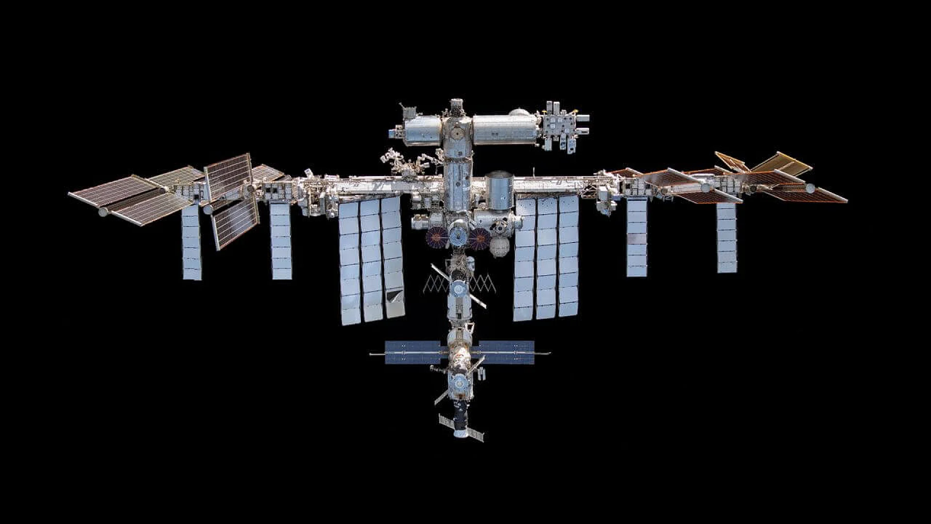 A high-resolution view of the International Space Station (ISS) against the black void of space, showing its expansive solar arrays and modular pressurized sections.