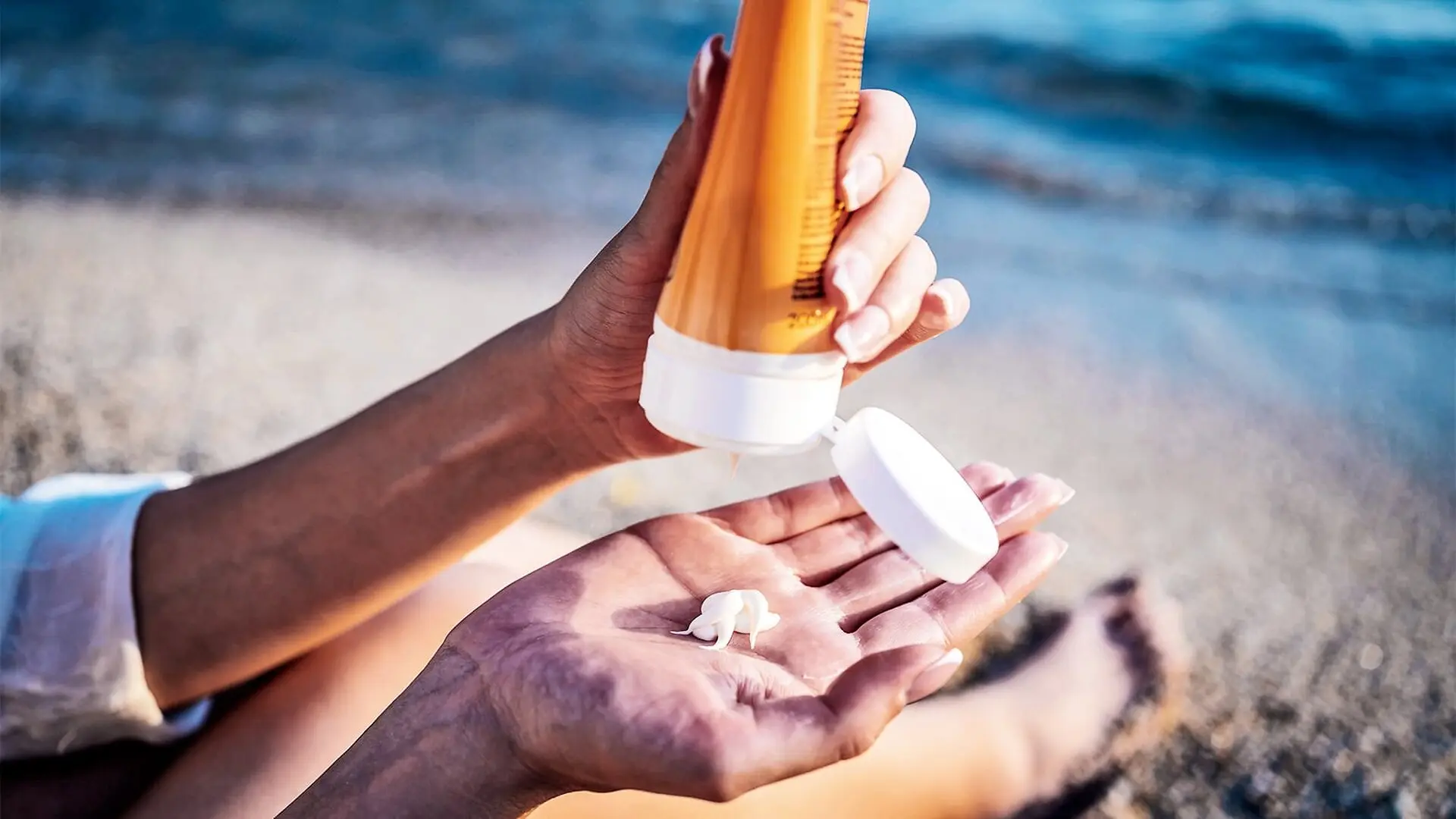 A woman squeezes sunscreen into her hand while at the beach.