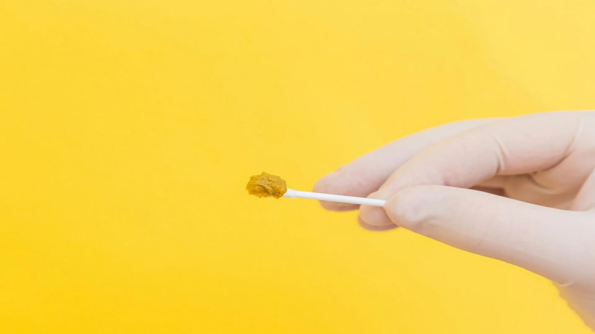 A doctor's hand in a white medical glove holds a stool sample on a stick on a yellow background. The medicine. Analysis. Cala. Infection. The close plan.