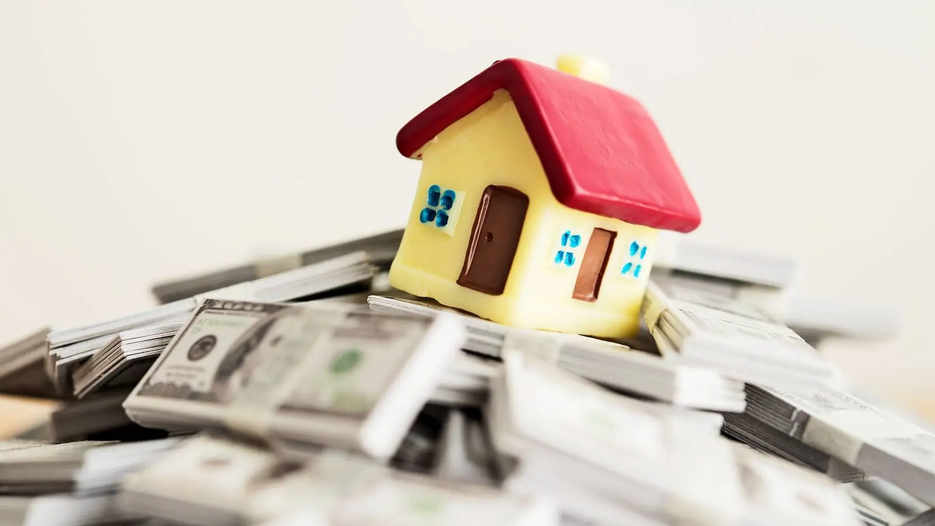 A small model of a house sits on stacks of cash.